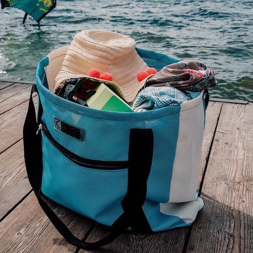 Geräumige Badetasche in Türkis-Weiß, gefüllt mit Sommer-Accessoires – der ideale Begleiter für See, Strand oder Pool.