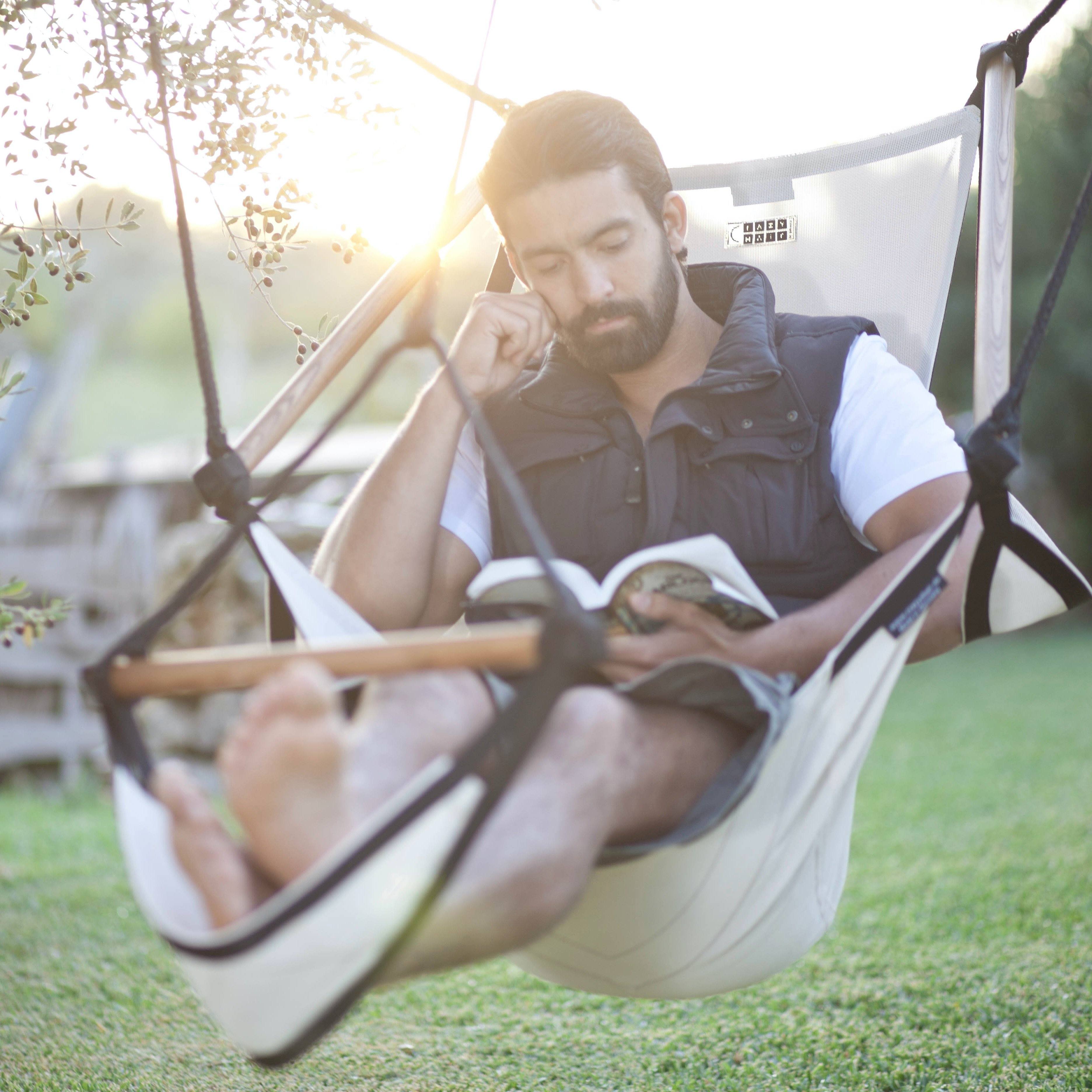 Mann liest entspannt in einem ergonomischen Hängesessel aus wetterfestem Material im Garten