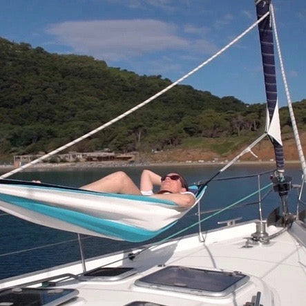 Person liegt entspannt in einer Hängematte, die mithilfe der Fockmanschette zwischen Mast und Fock auf dem Vorschiff einer Segelyacht aufgespannt ist – perfekte Entspannung mit sicherer Segelbefestigung
