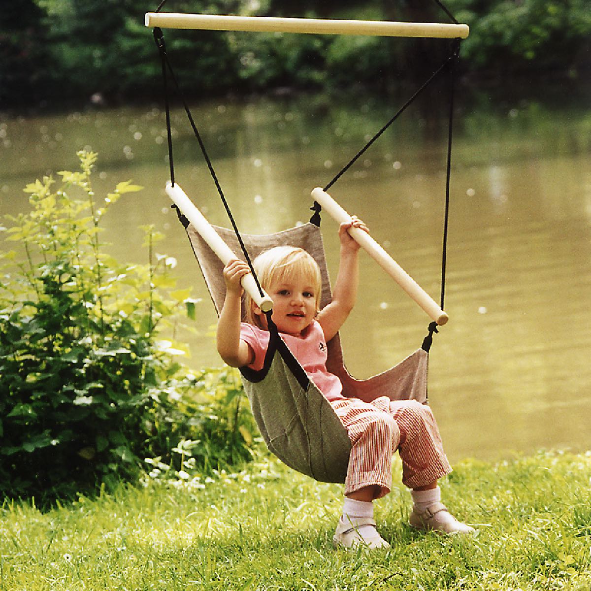 Kind sitzt entspannt im ergonomischen Kleinkinder-Hängesessel mit Holzstreben und atmungsaktivem Gewebe – ideal für den Garten oder Outdoor-Einsatz